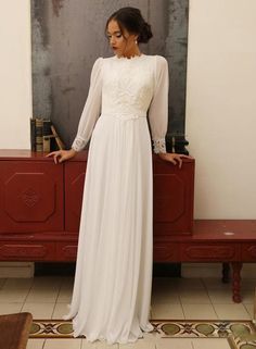 a woman standing in front of a painting wearing a long white dress with sheer sleeves