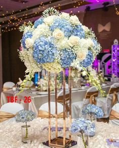 blue and white flowers are in a tall vase on a table at a wedding reception