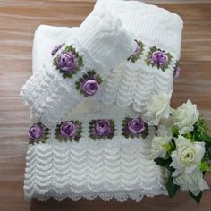 two white towels with purple flowers on them next to a bouquet of white and green flowers