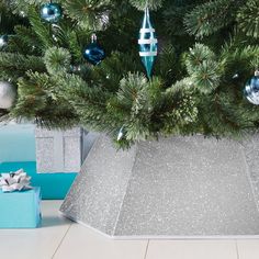 a christmas tree with presents under it and a blue present box underneath the fir tree