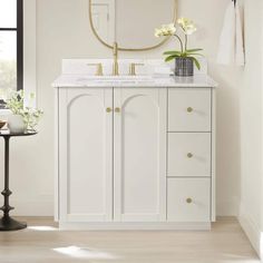 a white bathroom vanity with gold accents and mirror above it, along with a round mirror on the wall