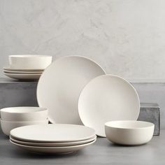 white plates and bowls stacked on top of each other in front of a gray wall