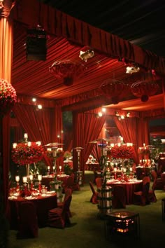 a room filled with lots of tables and chairs covered in red cloths, surrounded by candles