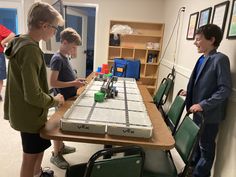 three boys standing around a table with a board game on it