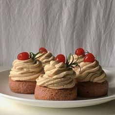 three cupcakes with cream frosting and cherries on top sit on a white plate