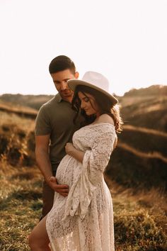 a pregnant woman in a white dress and hat standing next to a man