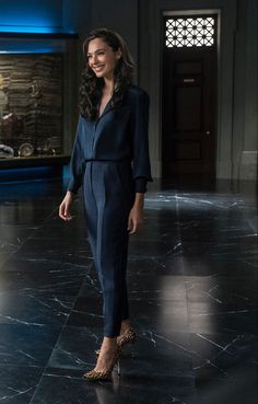 a woman in a black jumpsuit and leopard print heels standing on a marble floor