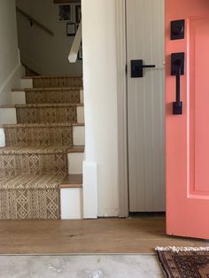 a pink door and some stairs in a house with carpet on the floor next to it