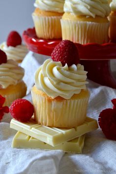 cupcakes with white chocolate frosting and raspberry toppings on a red plate