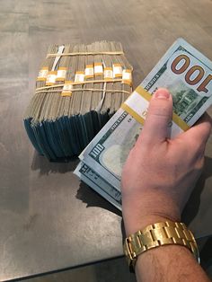 a person holding money in their hand next to some stacks of cash on a table