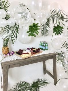 a table topped with lots of food next to balloons and palm leaves on the wall