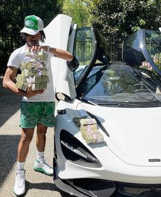 a man standing next to a white sports car with stacks of money in his pocket