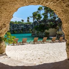 lounge chairs are lined up on the beach under an archway that leads to a lagoon