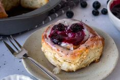 a pastry with blueberries and cream on it sitting next to a bowl of fruit