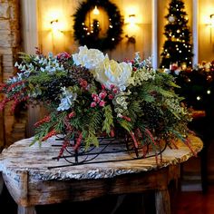 a table topped with flowers and greenery on top of a wooden table next to a christmas tree