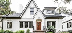 a white brick house with black trim and windows on the front door is surrounded by greenery