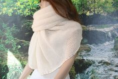 a mannequin wearing a white shawl in front of a waterfall