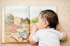 a baby laying on the floor next to an open book with winnie the pooh