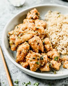 a white bowl filled with chicken and rice next to chopsticks on a table