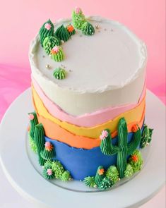 a multi layer cake with frosting and cactus decorations on it's sides, sitting on a white plate