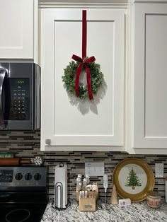 a christmas wreath hangs on the wall above a stove top oven in a kitchen with white cabinets and granite countertops