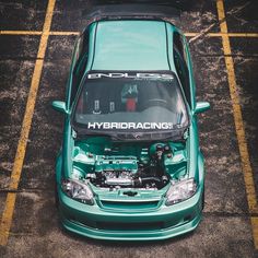 the front end of a green car parked in a parking lot with it's hood open