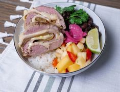 a bowl filled with meat, rice and fruit on top of a white table cloth