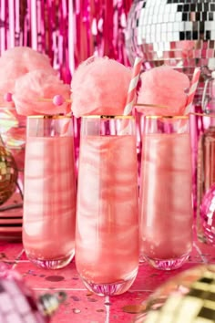 three glasses filled with pink liquid on top of a table next to confetti