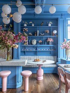 a kitchen with blue walls, pink stools and flowers in vases on the counter