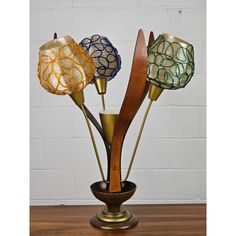 three decorative glass flowers in a vase on a wooden table next to a white brick wall