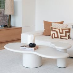 a living room with white couches and pillows on the table in front of it