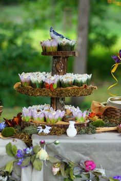 cupcakes are stacked on top of each other at a table with flowers and greenery