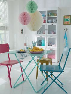 a dining table with three chairs and some paper lanterns hanging from it's ceiling