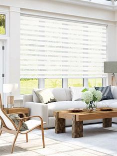 a living room filled with white furniture and windows covered in roman blind shades on top of them