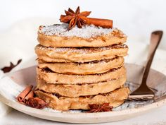 a stack of pancakes covered in powdered sugar with cinnamon and star anise on top