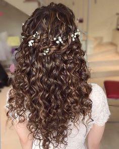 the back of a woman's head with long curly hair and flowers in her hair