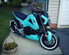 a blue motorcycle parked in front of a house next to a basket with flowers on it