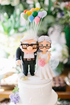 a wedding cake with a couple on top and balloons in the shape of people standing next to each other