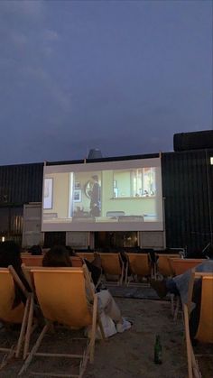 people are sitting in chairs watching a movie on the big screen outside at night time