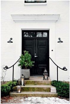 a white house with a black door and steps leading up to the front door is lit by lanterns