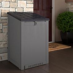 an outdoor trash can sitting in front of a brick wall next to a potted plant