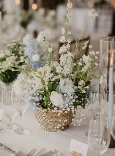 the table is set with white and blue flowers in vases, silverware, and wine glasses