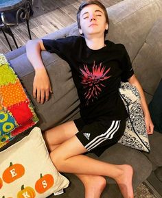 a young boy laying on top of a gray couch next to pillows and pumpkins