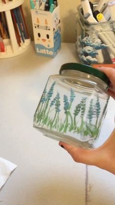 a person holding a jar with some flowers in it and writing on the inside of it