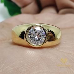 a gold ring with a diamond in the center on someone's hand and green leaves behind it