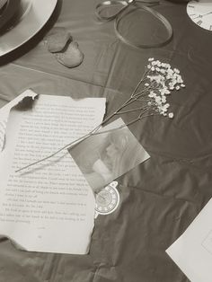 a table topped with papers and flowers on top of a cloth covered table next to plates