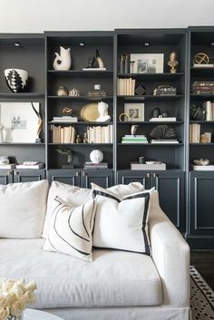 a white couch sitting in front of a book shelf filled with books and vases