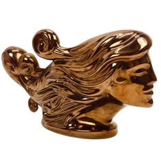 a gold colored sculpture of a woman's head with long hair and eyes closed