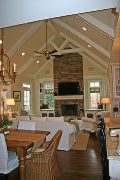 a large open concept living and dining room area with wood floors, vaulted ceiling, stone fireplace