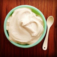 a green bowl filled with whipped cream next to a white spoon on top of a wooden table